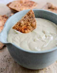 a blue bowl filled with white sauce and a tortilla chip sticking out of it