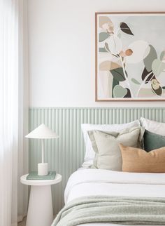 a bed with white sheets and pillows in a bedroom next to a painting on the wall