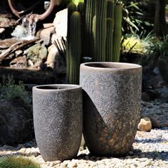 two large cement pots sitting next to each other on top of a gravel ground near cactuses