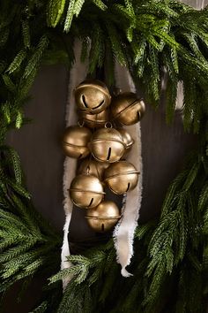 a wreath with bells hanging from it's center surrounded by evergreen leaves and pine cones