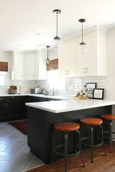 a kitchen with black and white cabinets, an island countertop and three stools