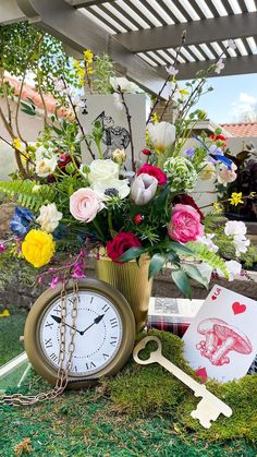 an arrangement of flowers in a vase with a clock on the ground next to it