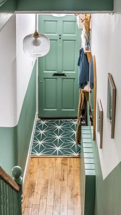 a hallway with green doors and wooden flooring next to a light fixture hanging from the ceiling