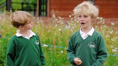 two young boys standing next to each other in front of some grass and flowers on a sunny day