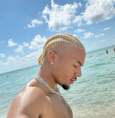 a man standing on top of a sandy beach next to the ocean with braids in his hair