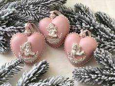 three pink heart shaped ornaments sitting on top of a table next to pine cones and branches