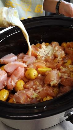 someone pouring milk into a slow cooker filled with food