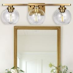 a bathroom vanity with three lights and a mirror on the wall next to flowers in vases