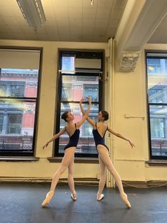 two ballerinas in black leotards are dancing