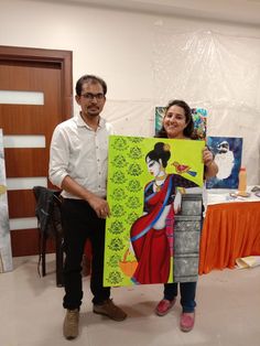 a man and woman standing next to each other holding paintings