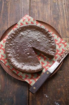 a chocolate cake sitting on top of a wooden table next to a knife and fork