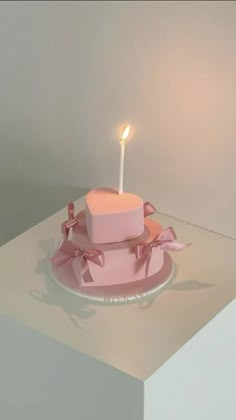 a pink heart shaped cake with a single candle on it's top sitting on a plate