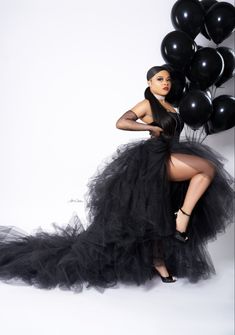 a woman in a black dress is posing for the camera with balloons behind her,