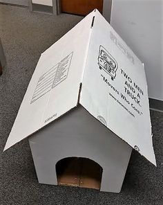 a cardboard box that is sitting on the floor with a dog house inside it and its door open