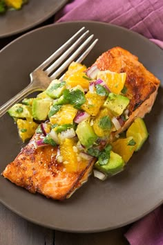 two plates with salmon, avocado and mango salsa on them next to a fork