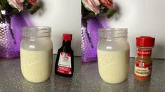 two jars filled with liquid sitting on top of a counter next to flowers and condiments