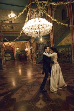 a man and woman are dancing in an ornate room with chandelier hanging from the ceiling