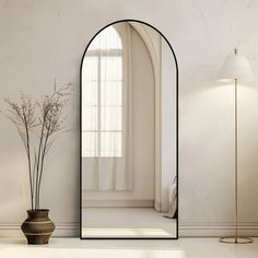 an arch shaped mirror sitting on top of a floor next to a vase and lamp