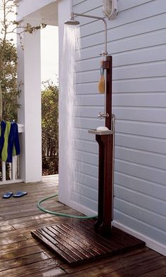 an outdoor shower on a wooden deck next to a white house with blue and green towels