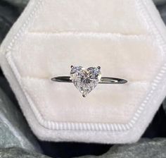 an engagement ring with a heart shaped diamond on it's side in a velvet box