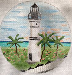 a cross stitch picture of a lighthouse on the beach with palm trees in the background