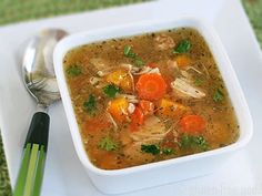 a bowl of soup with carrots, chicken and celery on a white plate