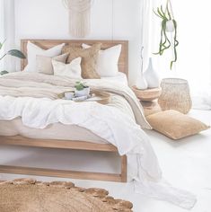 a bed with white sheets and pillows in a bedroom next to a plant on the floor