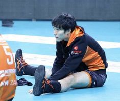 a man sitting on the ground with his feet up in front of him, wearing shorts and an orange hoodie