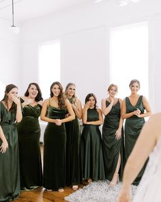 a group of women standing next to each other in front of a mirror wearing green dresses