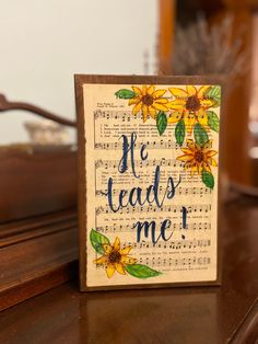 a wooden block with the words he leads me written on it and sunflowers