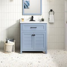 a bathroom with a blue vanity and white tiled walls, along with a basket on the floor