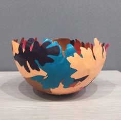 a colorful bowl sitting on top of a white table next to a gray and grey wall