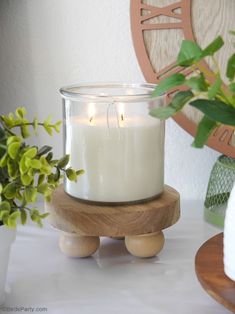 a white candle sitting on top of a wooden stand next to a potted plant