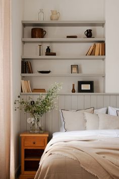 a bed with white sheets and pillows in front of a book shelf filled with books