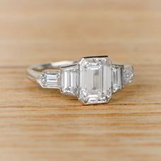 an emerald and diamond ring sitting on top of a wooden table