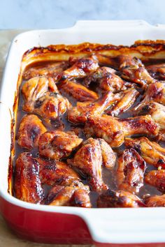 a red casserole dish filled with chicken wings covered in brown gravy