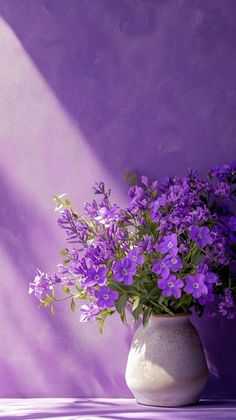 a white vase filled with purple flowers on top of a table