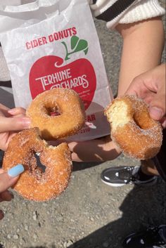 two people holding donuts in their hands with powdered sugar on them and an apple bag behind them