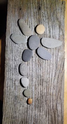 a cross made out of rocks sitting on top of a piece of wood with leaves