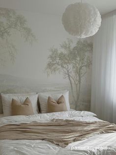 a bed with white sheets and pillows in front of a wallpapered tree mural