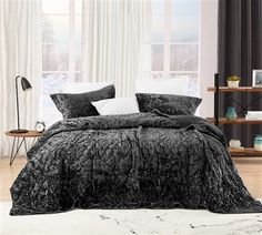 a bed with black comforter and pillows in a room next to a white rug