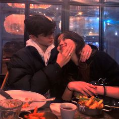 two people sitting at a table with food in front of them and one woman covering her mouth