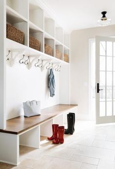 a white entryway with wooden bench and coat rack filled with rain boots next to glass doors