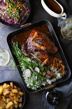 a roasting pan filled with meat and vegetables next to two glasses of wine on a table