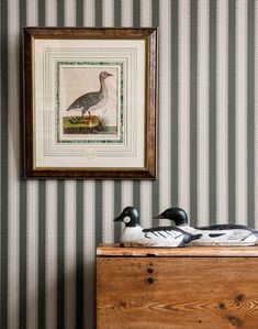 two ducks sitting on top of a wooden chest in front of a striped wallpaper