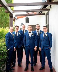 a group of men standing next to each other wearing blue suits and bow ties on a patio