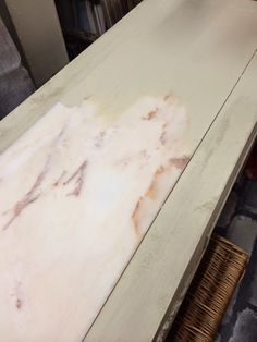 a white table with some brown stains on it and a chair in the back ground