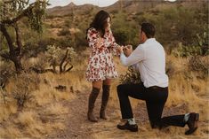 a man kneeling down next to a woman in a dress and knee high boots on a dirt road