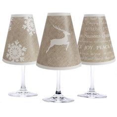 three wine glasses sitting next to each other on top of a white table cloth covered lamp shade