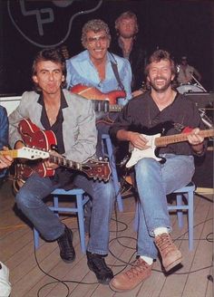 four men are sitting in chairs playing guitars